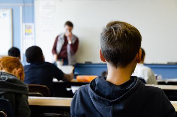 Children sitting in a classroom facing teacher at the front by white board