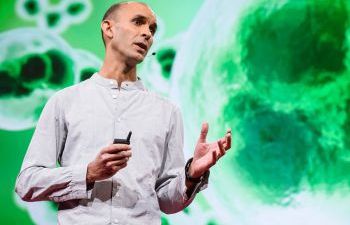 Anil Seth delivering a talk with a bright green backdrop