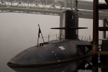 A military submarine partly submerged in dock with foggy city skyline in background