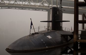 A military submarine partly submerged in dock with foggy city skyline in background