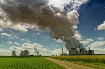 A rural power plant set in green fields sends plumes of smoke into the sky