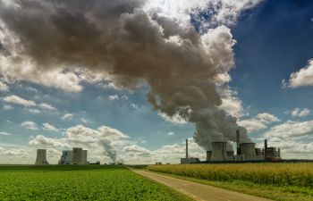 A rural power plant set in green fields sends plumes of smoke into the sky