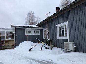A blue one storey home fitted with a heat pump surrounded by heavy snow