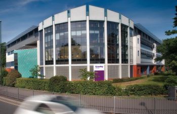 A view across the road of Crawley College - a modern looking glass fronted building set behind a small hedgerow