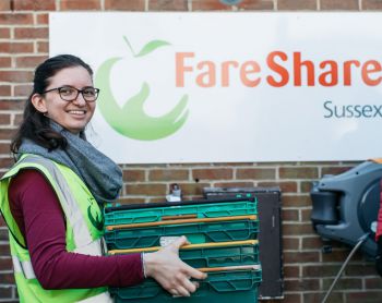 University of Sussex student Anna Maukner, wearing a high vis jacket, is carrying plastic containers in front of the FareShare logo