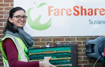 University of Sussex student Anna Maukner, wearing a high vis jacket, is carrying plastic containers in front of the FareShare logo