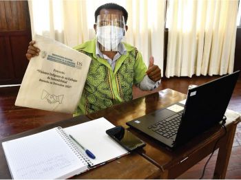 A student sitting in front of a laptop wearing PPE holding up a branded UNIA bag and giving a thumbs up