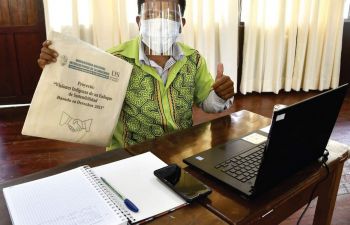 A student sitting in front of a laptop wearing PPE holding up a branded UNIA bag and giving a thumbs up