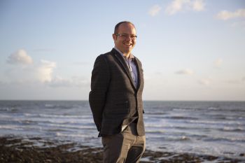 Photo of Prof Benjamin Sovacool standing on a beach with the sea behind him