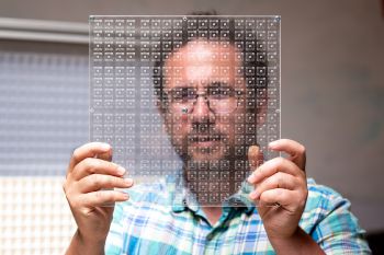 Dr Gianluca Memoli is dressed in a brightly coloured check shirt and is holding a piece of transparent material across his face