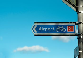 A blue sign pointing the route of a cycle lane to an airport