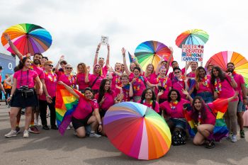 A large group of university students wearing bright pink t-shirts and some holding rainbow umbrellas