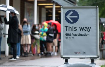 Sign for a Covid-19 vaccination clinic, with blurred image behind of students queueing