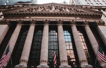 Image looks up at the facade of the US stock exchange with its large columns and numerous US flags