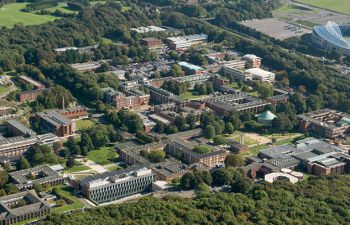 An aerial view of the University of Sussex campus showing the buildings among the green of trees