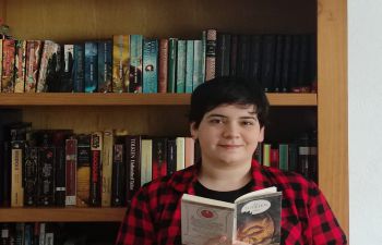 Student Ambassador Angeles Gonzalez reading a book by a bookcase