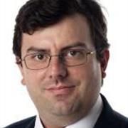 Close-up head shot of Prof Xavier Calmet with dark hair, glasses and a white shirt and dark suit just visible