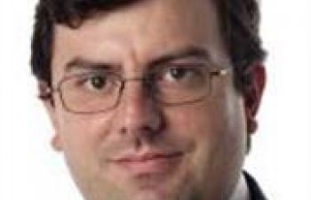 Close-up head shot of Prof Xavier Calmet with dark hair, glasses and a white shirt and dark suit just visible