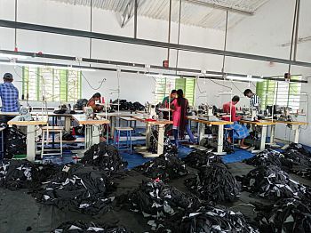 A room of a textiles factory with people working and clothes on the floor