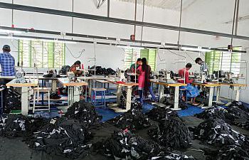 A room of a textiles factory with people working and clothes on the floor