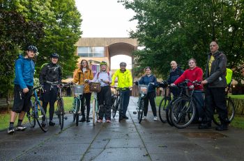 A group of nine staff and students stands together outside of Falmer House with their bicycles, after cycling together to campus