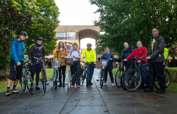 A group of nine staff and students stands together outside of Falmer House with their bicycles, after cycling together to campus