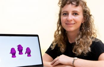 Claire Lancaster is wearing a black top and sits beside a computer screen displaying three purple images on a white background