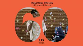 photo of alumnus Jordi Carter in Mandela Hall looking up at confetti falling, with 60 years of Sussex text and logo in foreground