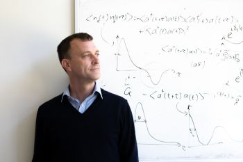 Photograph of University of Sussex Professor of Physics, Jacob Dunningham in front of a whiteboard
