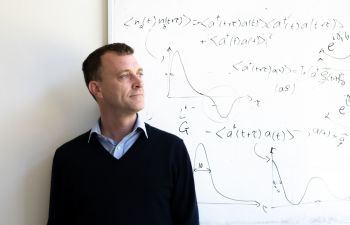 Photograph of University of Sussex Professor of Physics, Jacob Dunningham in front of a whiteboard