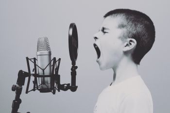 A child with a shaved head shouts into a microphone in black-and-white