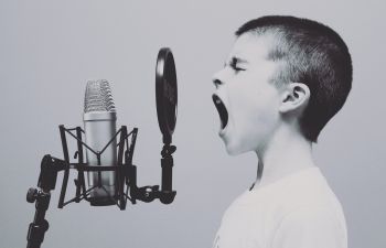 A child with a shaved head shouts into a microphone in black-and-white