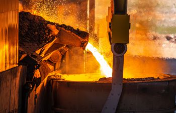 Hot molten metal is poured into a large container at a steel factory