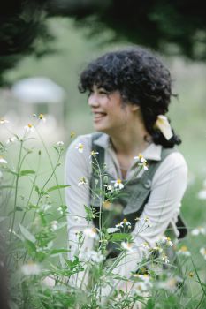 A woman smiling, sat in a field of flowers