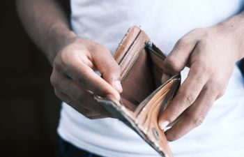 A man opens up his brown leather wallet to reveal that it is empty