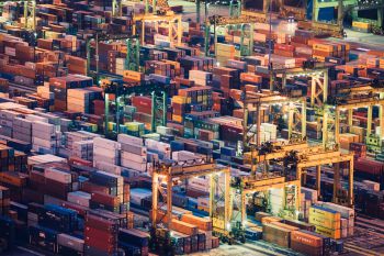 Aerial view over a busy port at night with thousands of shipping containers illuminated by floodlights