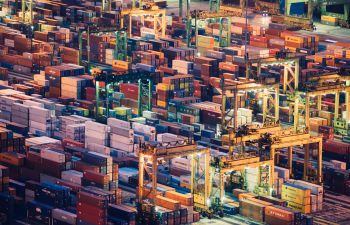 Aerial view over a busy port at night with thousands of shipping containers illuminated by floodlights