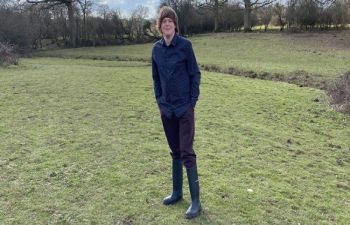James stands in a rural green space in front of a line of trees