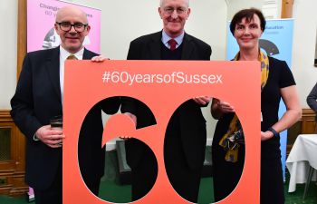 Two men and a woman face the camera holding a carboard cut-out of the number 60