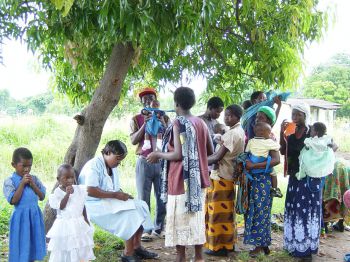 A group of people in Africa pictured under a tree, including men, women and children