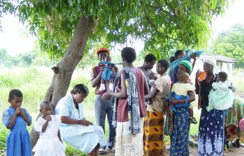 A group of people in Africa pictured under a tree, including men, women and children