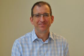 Prof Chris Pepper smiling in a check shirt in front of a plain wall