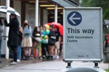 A sign directs towards a vaccination centre while people queue up in the background