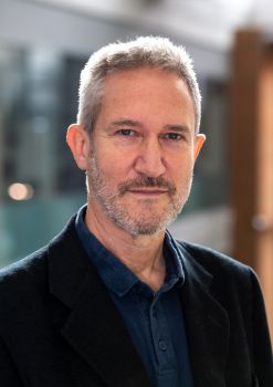 Head and shoulders image of Dr Matthew Lockwood sporting short light-grey hair and stubble and wearing a blue polo shirt and a navy jacket