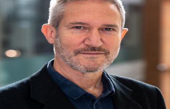 Head and shoulders image of Dr Matthew Lockwood sporting short light-grey hair and stubble and wearing a blue polo shirt and a navy jacket