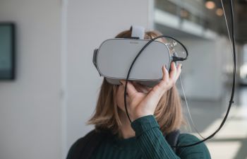 A woman wearing a green sweater pulls a pair of virtual reality glasses over her head