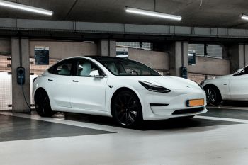 A white electric vehicle is parked in a multi-storey car park and is plugged in to charge