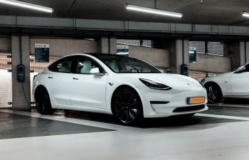 A white electric vehicle is parked in a multi-storey car park and is plugged in to charge