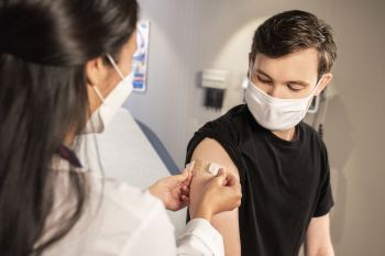 A doctor gives a Covid-19 vaccine injection to a young man wearing a black shirt in a clinical setting