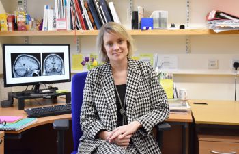 Dr Jessica Eccles pictured on a chair in her office in front of a computer with a brain scan image